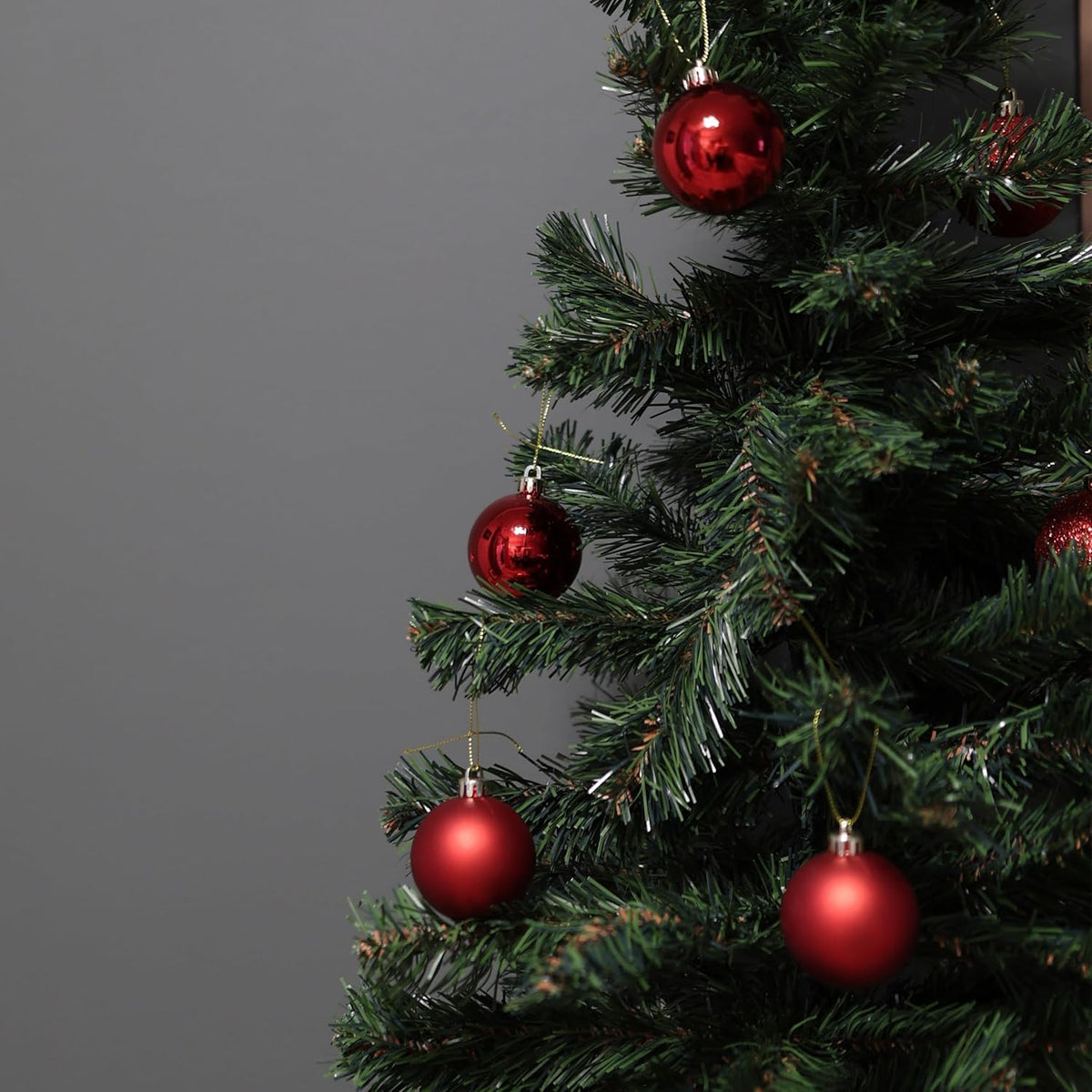 Close-up of a Christmas tree with red ornaments against a gray background