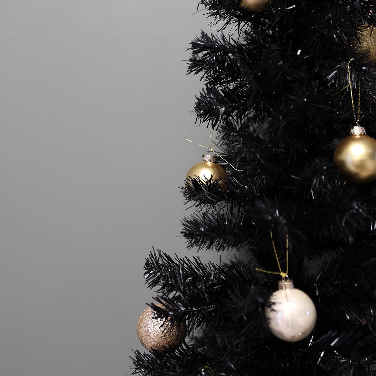 Black Christmas tree with gold and silver ornaments on a gray background