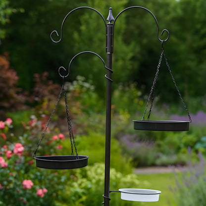 Black metal bird feeder stand with three hanging bird baths in a garden setting.