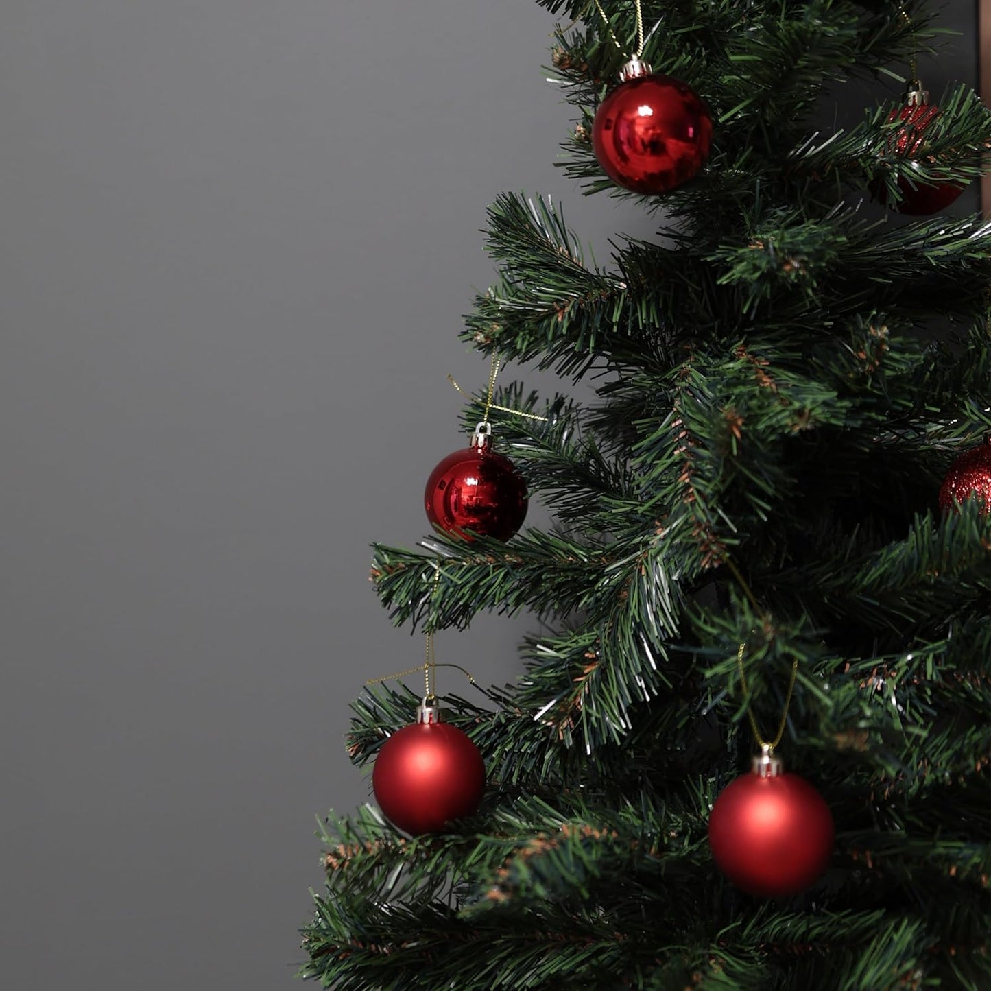 Close-up of a Christmas tree with red ornaments against a gray background