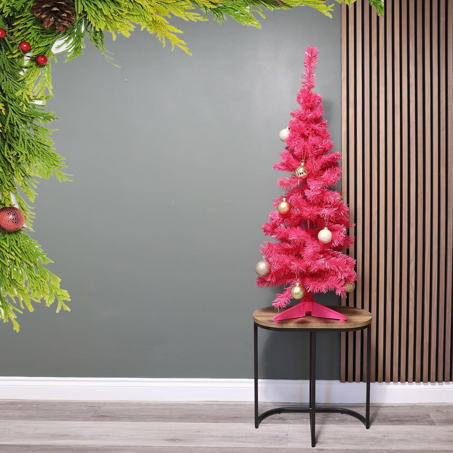 Pink Christmas tree with decorations on a small round table against a gray wall.