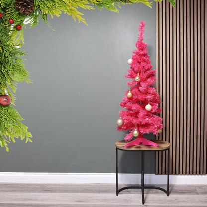Pink Christmas tree with decorations on a small round table against a gray wall.