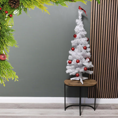 White Christmas tree with red ornaments on a wooden table against a gray wall.